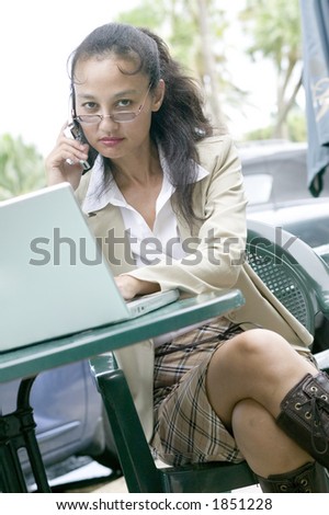 An attractive young asian business woman keeps in touch whilst on the go with the latest technology.