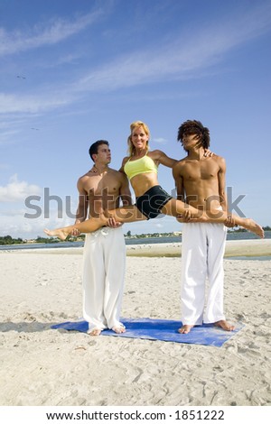 Two muscular young men lift an attractive young woman into the splits position on the beach