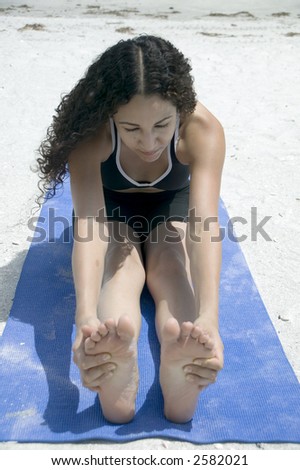 A young hispanic woman in black sports outfit  practices Yoga on the beach