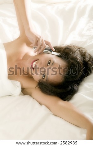 An attractive young asian woman talks on her cell phone whilst still in bed