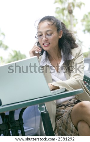 An attractive young asian business woman keeps in touch whilst on the go with the latest technology.