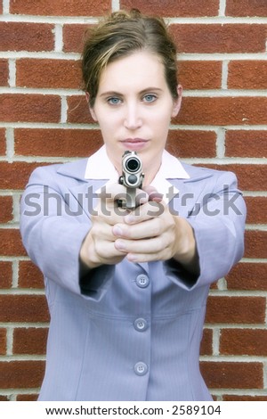 A woman in a business suit points a gun at the camera