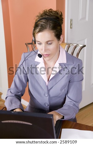 A young woman in business suit talking on a headset working from home