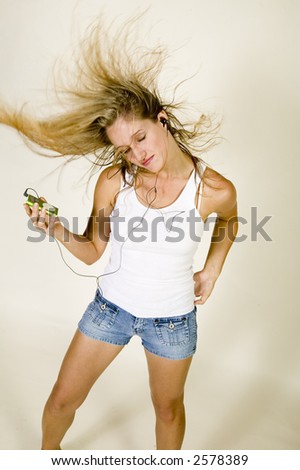 young attractive blond woman in white tee shirt and denim jeans listens to music on her MP3 player