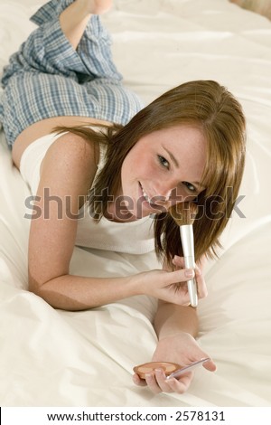 very attractive young teen girl in pajamas laying on her bed putting on her make up