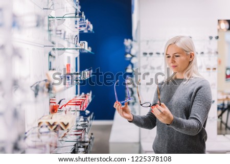 Woman comparing glasses at optic store. Eyewear shopping, correction glasses.