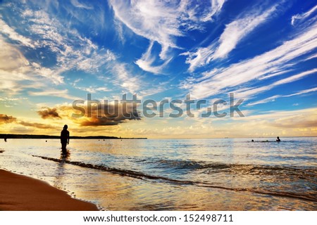 Woman standing in calm ocean under dramatic sunset sky. Summertime