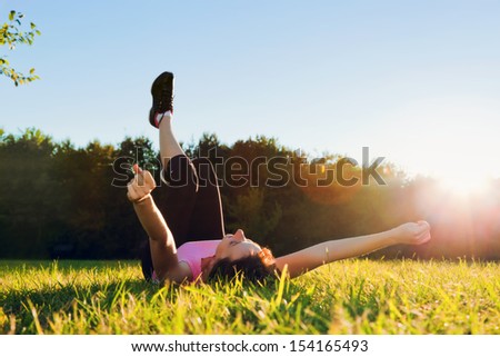Young pretty woman lying and streching herself on the grass at summer sunset. Relaxation, balance and harmony.