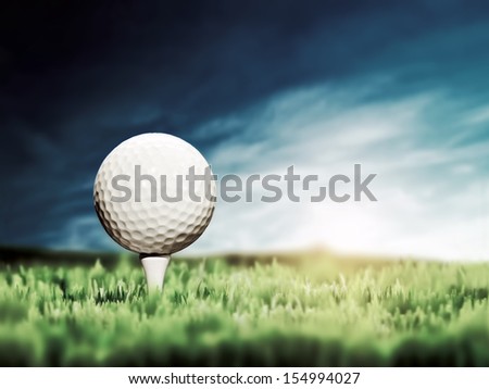 Golf ball placed on white golf tee on green grass golf course. Moody sunny sky.