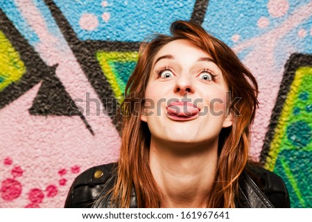 Stylish girl poking out her tongue to the camera against colorful graffiti wall.