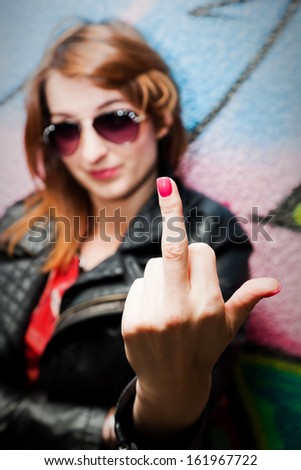 Stylish fashionable girl showing fuck off middle finger gesture against colorful graffiti wall.