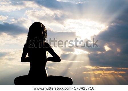 A silhouette of a woman sitting in yoga position, meditating against sunset sky. Zen, meditation