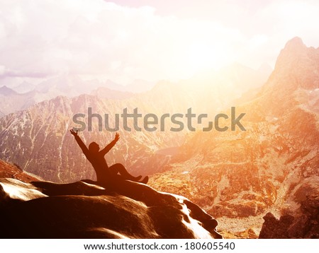 A happy man sitting on the peak of a mountain with hands raised admiring breathtaking view at sunset A happy man sitting on the peak of a mountain with hands raised admiring breathtaking view at sunset
