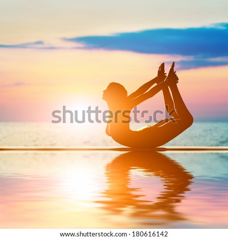 A silhouette of a woman in bow yoga position, meditating against sunset sky. Zen, meditation