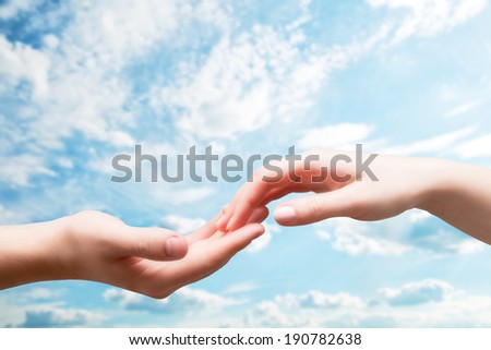 Man and woman hands touch in gentle, soft way on blue sunny sky. Concepts of connection, hope, faith, help, love.