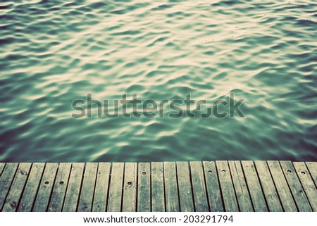 Grunge wood boards of a pier over ocean with rippling waves. Vintage background