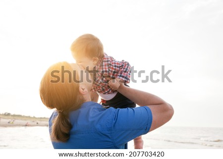 Young father holding his child up in the air on the beach and kissing with love. Son and parent bond