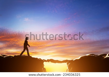 Man walking over precipice between two mountains, another man serving as a bridge. Sunset, business conceptual