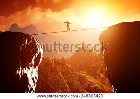 Man walking and balancing on rope over precipice in mountains at sunset. Concept of business, risk taking, challenge, concentration.