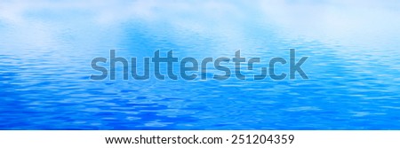 Clean water background with calm waves. Blue sky reflection. Banner, panorama.