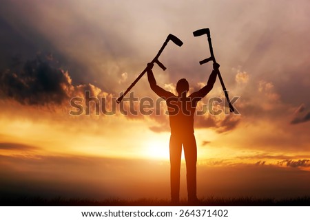A disabled man raising his crutches at sunset. Positive concept of cure, recovery, medical miracle, hope, insurance etc.