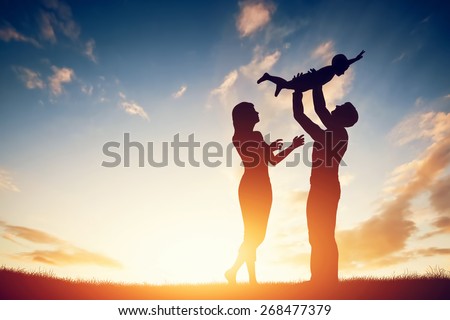 Happy family together, parents with their little child at sunset. Father raising baby up in the air.
