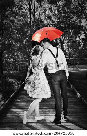 Young romantic couple in love flirting in rain, man holding red umbrella. Dating, romance, black and white