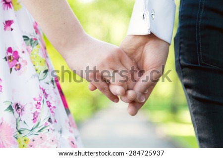 Holding hands close-up. Couple in love dating in summer park. Woman in dress and man wearing elegant shirt. View from the back. Date, fiance with fiancee, hand in hand concepts