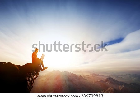Man working on notebook sitting on cliff on top of the mountains. Concepts of staying online everywhere, internet, freedom reception etc.