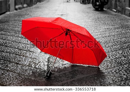 Red umbrella on cobblestone street in the old town. Wind, rain, stormy weather. Color in black and white conceptual, idea. Vintage, retro style.