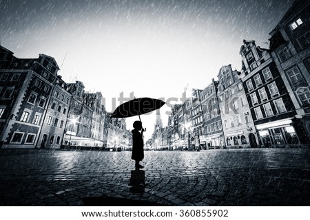 Child with umbrella standing alone on cobblestone old town in rain. Concept of being lost, lonely in a big world or exploring
