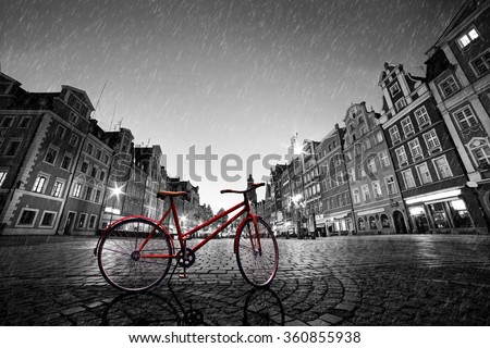 Vintage red bike on cobblestone historic old town in rain. Color in black and white. The market square at night. Wroclaw, Poland.