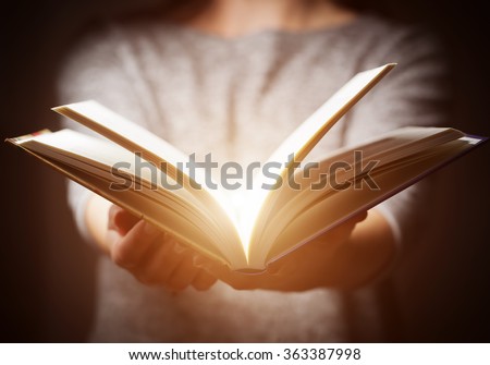 Light coming from book in woman\'s hands in gesture of giving, offering. Concept of wisdom, religion, reading, imagination.