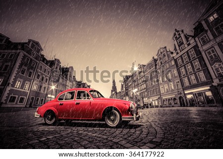Retro red car on cobblestone historic old town in rain. The market square at night. Wroclaw, Poland.