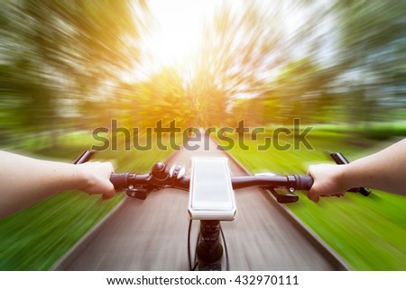 Riding a bike first person perspective. Smartphone attached to handlebar. Speed motion blur. Countryside road towards sun.