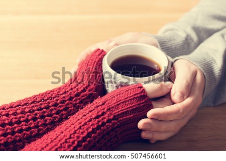 A couple in love warming hands with a hot mug of tea. Wearing cosy woollen jumpers.