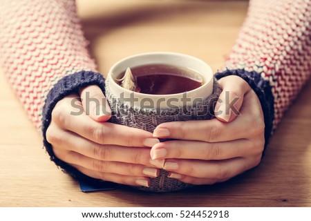 Hot mug of tea warming woman\'s hands in retro woollen jumper. Wooden table