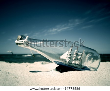 Bottle with ship inside lying on the beach. Conceptual image