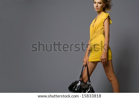 Attractive young fashion model in yellow dress with black bag.