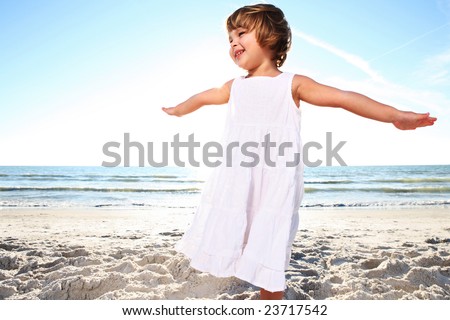 Small cute girl in white dress enjoying sunny day at the beach. Shoot against the sun.