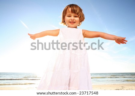 Happy little girl in white dress enjoying sunny day at the beach. Shoot against the sun.