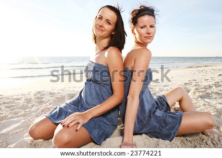 Two young attractive girls enjoying friendship at the sunny beach. Shoot against the sun.