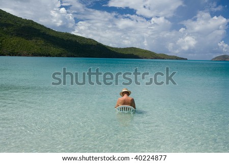 Older man in white hat sleeping on chair in tropical blue water.