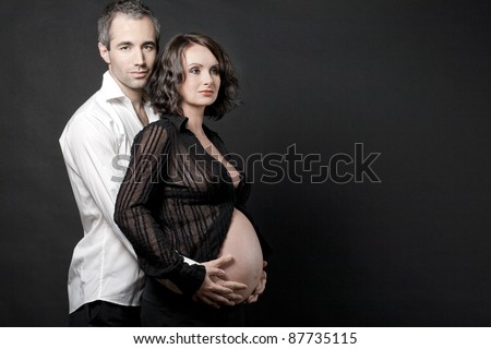 Handsome pregnant couple posing on dark background.