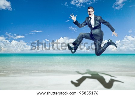 Young happy businessman jumps in black suit on tropical beach.