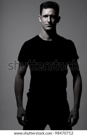 Young strong slim man in black t-shirt posing on gray background.