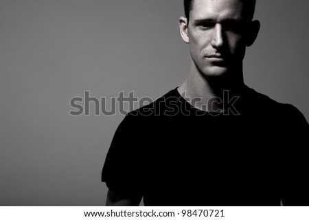 Young strong slim man in black t-shirt posing on gray background.