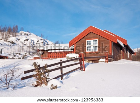 Norwegian small mountain cottage at a sunny winter day with snow in december with a simple fence of wood in the foreground