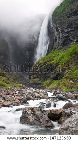 Norwegian waterfall Vettisfossen with northern europe highest free fall during a misty day with a river in the foreground