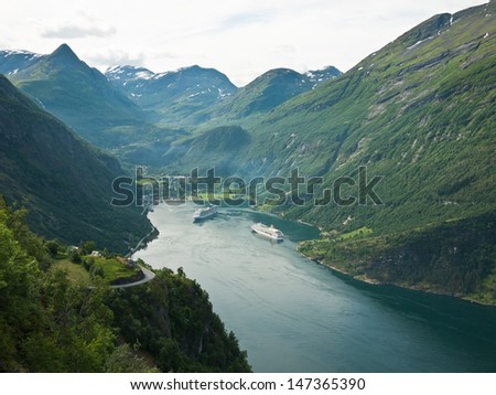 Viewpoint towards the end of Geirangerfjord in Norway with the small village Geiranger at the end and cruise ships anchored just outside the village